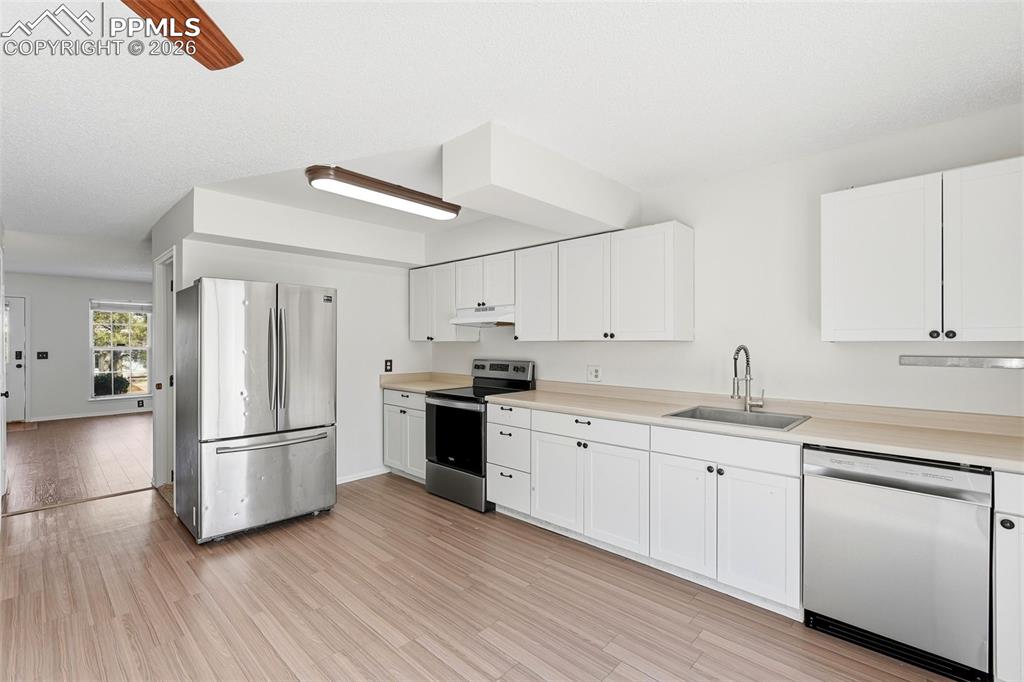 Kitchen featuring stainless steel appliances, light countertops, white cabinetry, light wood-style floors, and a ceiling fan