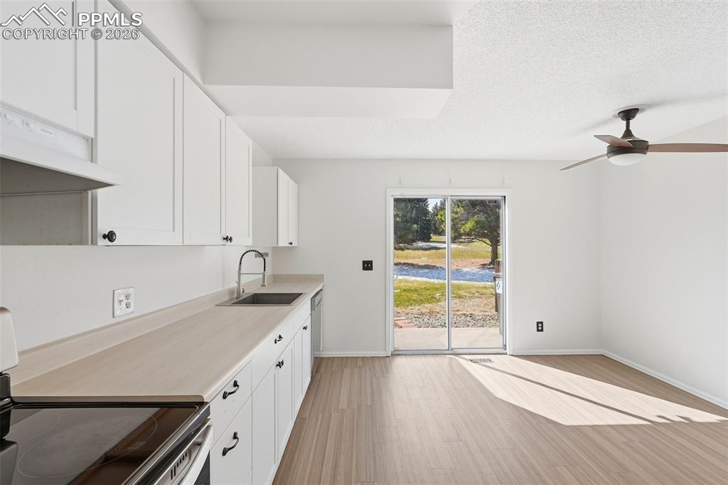 Kitchen with stainless steel appliances, white cabinets, light countertops, ceiling fan, and light wood finished floors