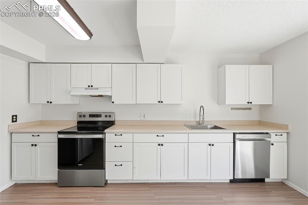 Kitchen with stainless steel appliances, light countertops, white cabinetry, and light wood-style floors