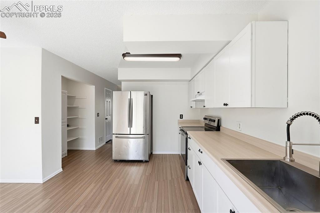Kitchen featuring light countertops, stainless steel appliances, white cabinets, light wood-style floors, and a textured ceiling