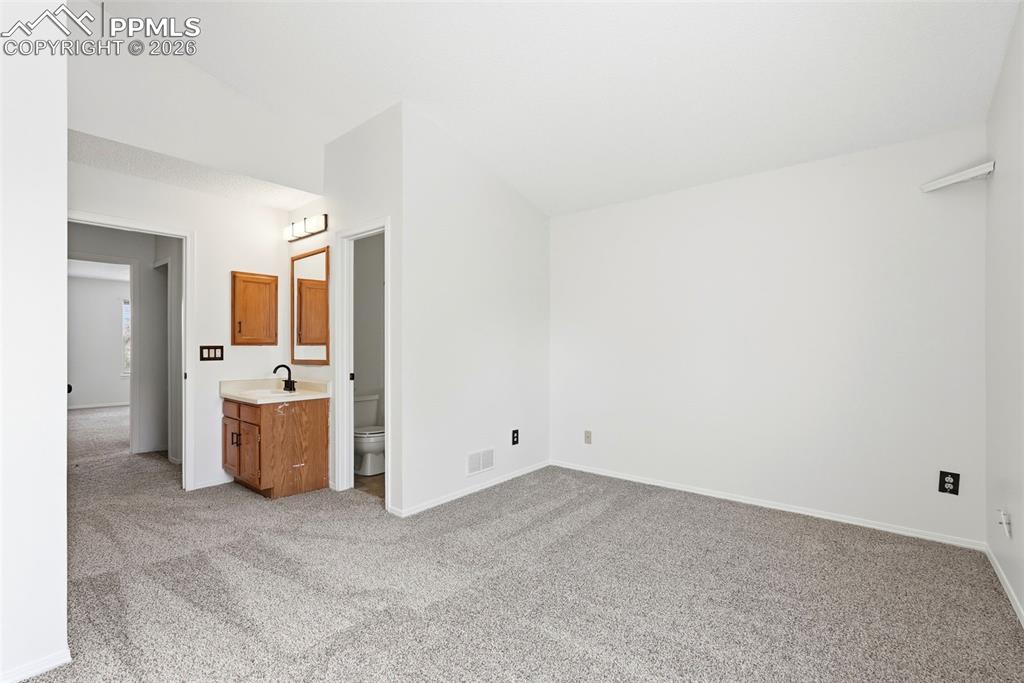 Unfurnished bedroom with lofted ceiling, light colored carpet, and connected bathroom