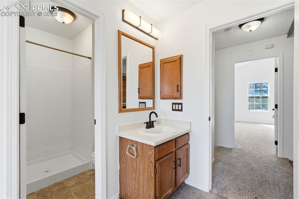 Full bath with vanity, a stall shower, light carpet, and a textured ceiling