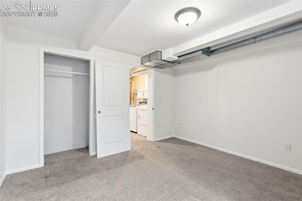 Unfurnished bedroom with washing machine and dryer, light carpet, a closet, and beam ceiling