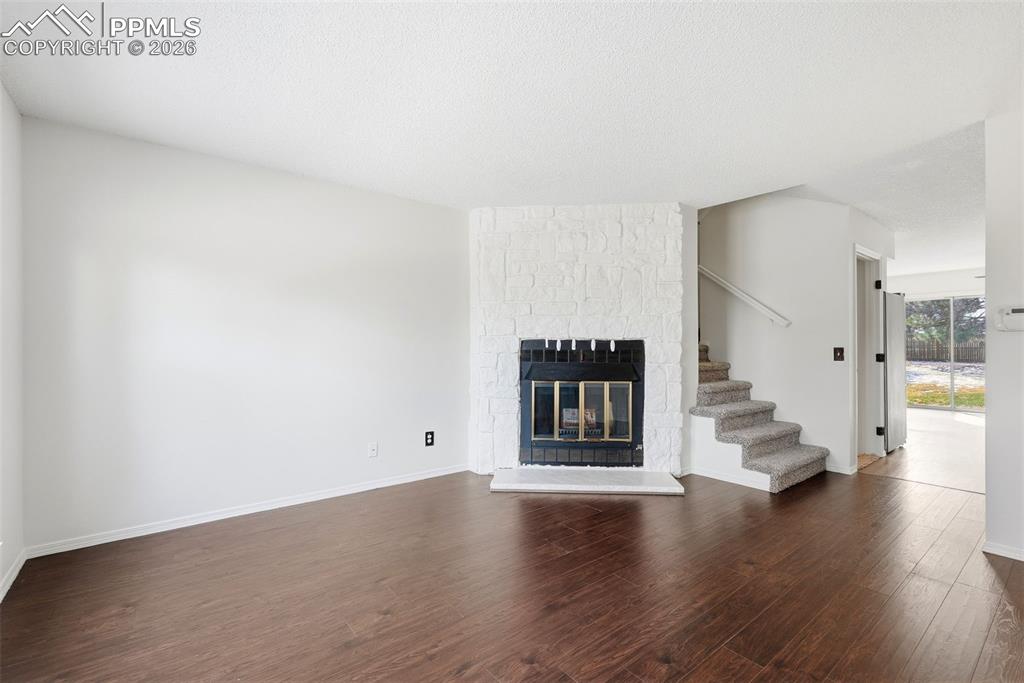 Unfurnished living room with dark wood finished floors, a fireplace, and a textured ceiling