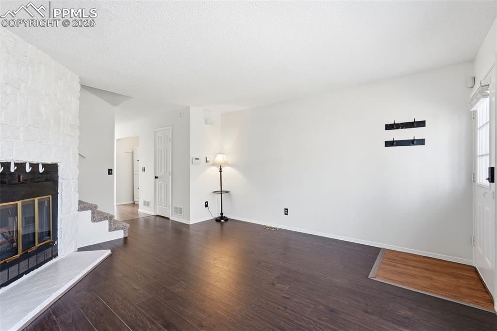 Unfurnished living room featuring dark wood-type flooring, a stone fireplace, and a textured ceiling