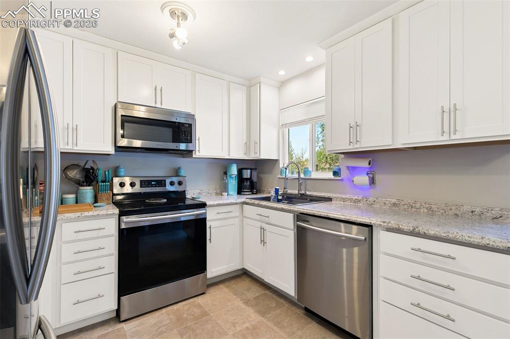 Kitchen with appliances with stainless steel finishes, recessed lighting, white cabinetry, and light stone counters
