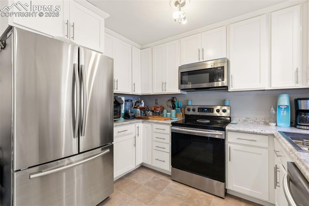 Kitchen with stainless steel appliances, white cabinetry, and light stone countertops