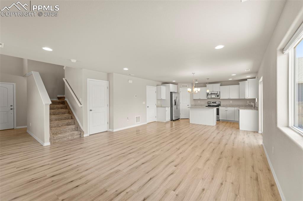 Unfurnished living room featuring stairway, light wood finished floors, recessed lighting, and a chandelier