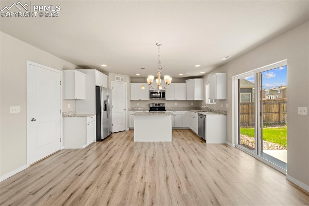 Kitchen with appliances with stainless steel finishes, a chandelier, light wood-type flooring, a kitchen island, and recessed lighting