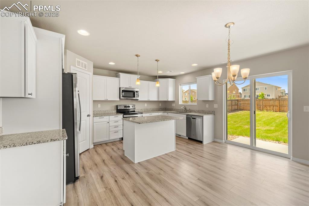 Kitchen featuring stainless steel appliances, light wood finished floors, a chandelier, a center island, and white cabinetry