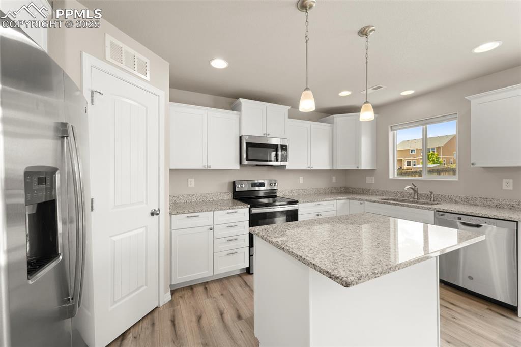 Kitchen featuring appliances with stainless steel finishes, light wood-type flooring, recessed lighting, a center island, and white cabinets