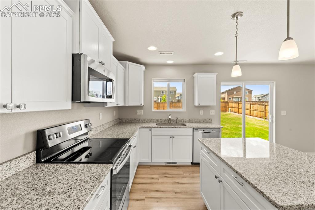 Kitchen featuring appliances with stainless steel finishes, white cabinetry, recessed lighting, light wood-type flooring, and light stone countertops