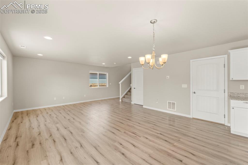 Unfurnished living room with stairs, light wood-style flooring, recessed lighting, and a chandelier