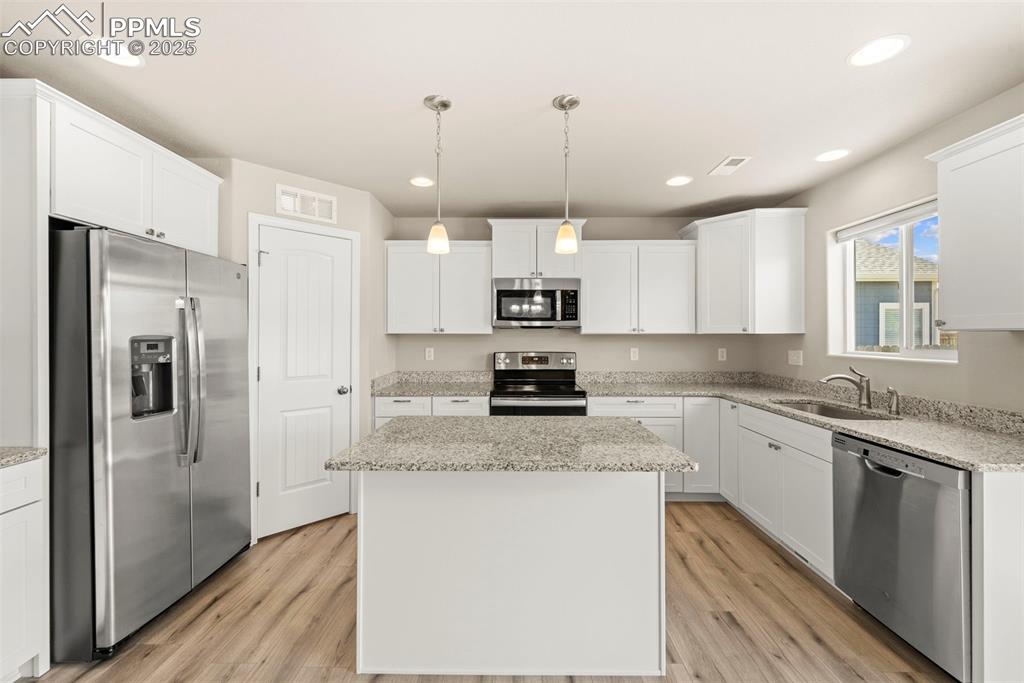 Kitchen featuring stainless steel appliances, a kitchen island, white cabinetry, light wood-style flooring, and recessed lighting