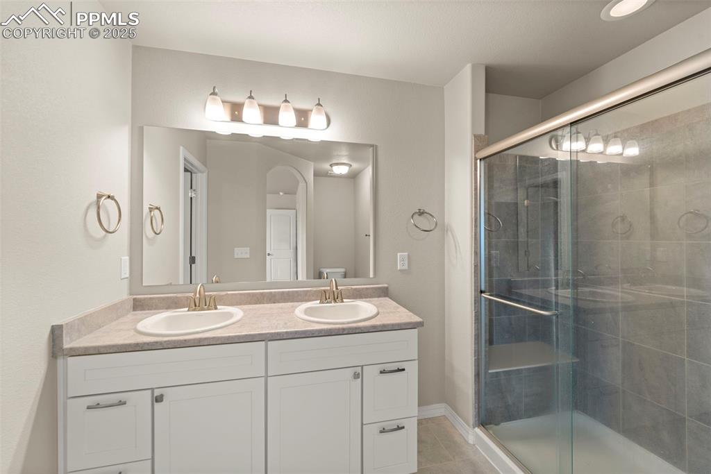 Bathroom with double vanity, a shower stall, and tile patterned flooring