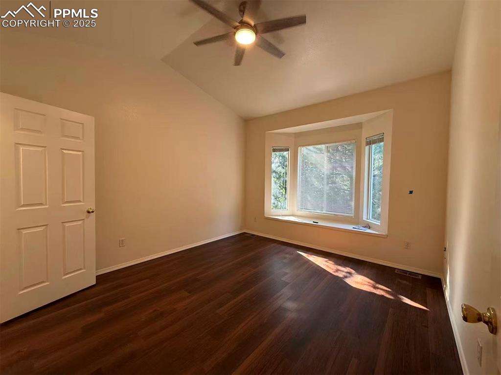 Empty room with dark wood finished floors, vaulted ceiling, and ceiling fan