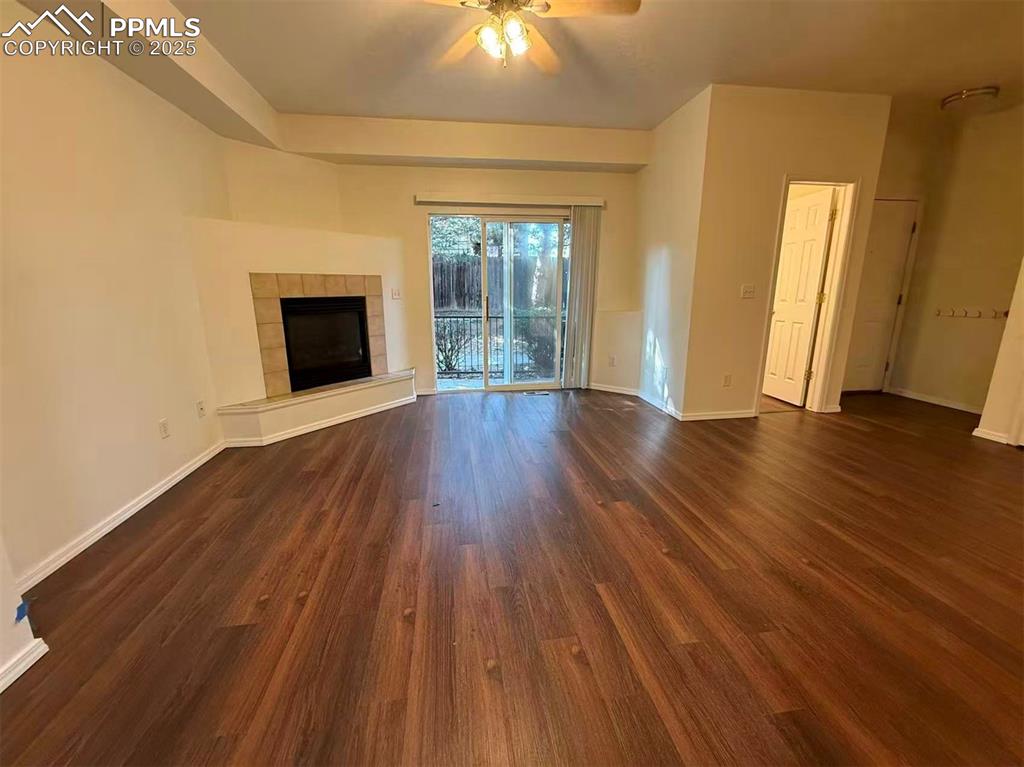 Unfurnished living room with a tile fireplace, dark wood-type flooring, and ceiling fan