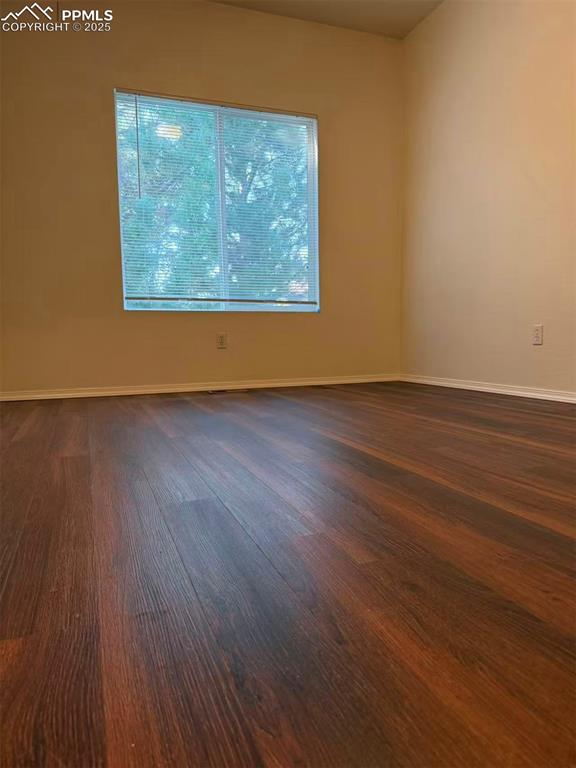 Spare room with baseboards and dark wood-type flooring