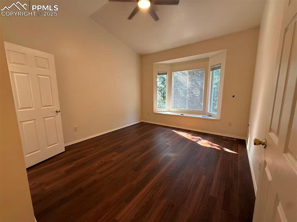 Unfurnished room featuring dark wood-type flooring, vaulted ceiling, and ceiling fan