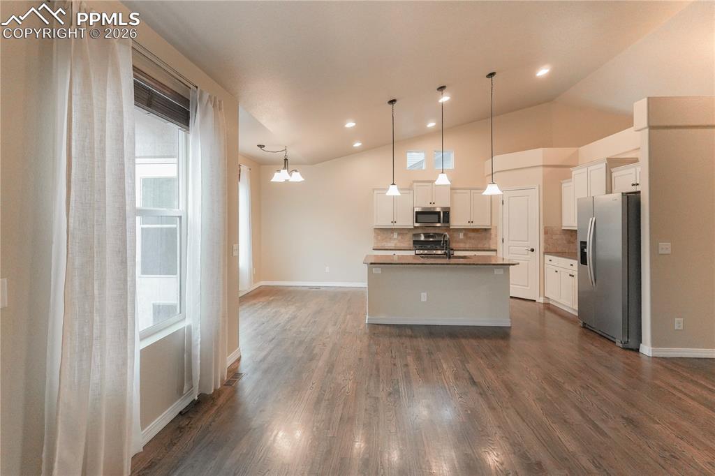 Kitchen featuring stainless steel appliances, white cabinets, vaulted ceiling, a center island with sink, and decorative backsplash