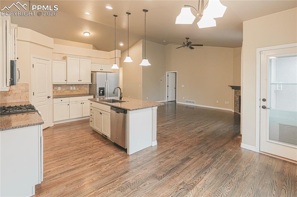 Kitchen featuring decorative light fixtures, tasteful backsplash, stainless steel appliances, lofted ceiling, and dark stone countertops