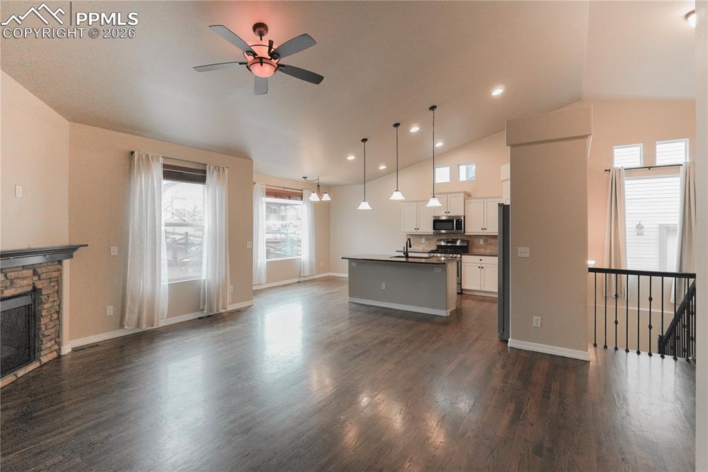 Unfurnished living room with vaulted ceiling, recessed lighting, dark wood-type flooring, ceiling fan, and a fireplace