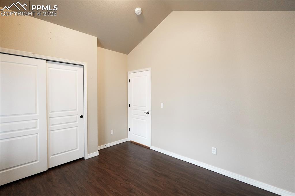 Unfurnished bedroom featuring a closet, dark wood-style floors, and vaulted ceiling