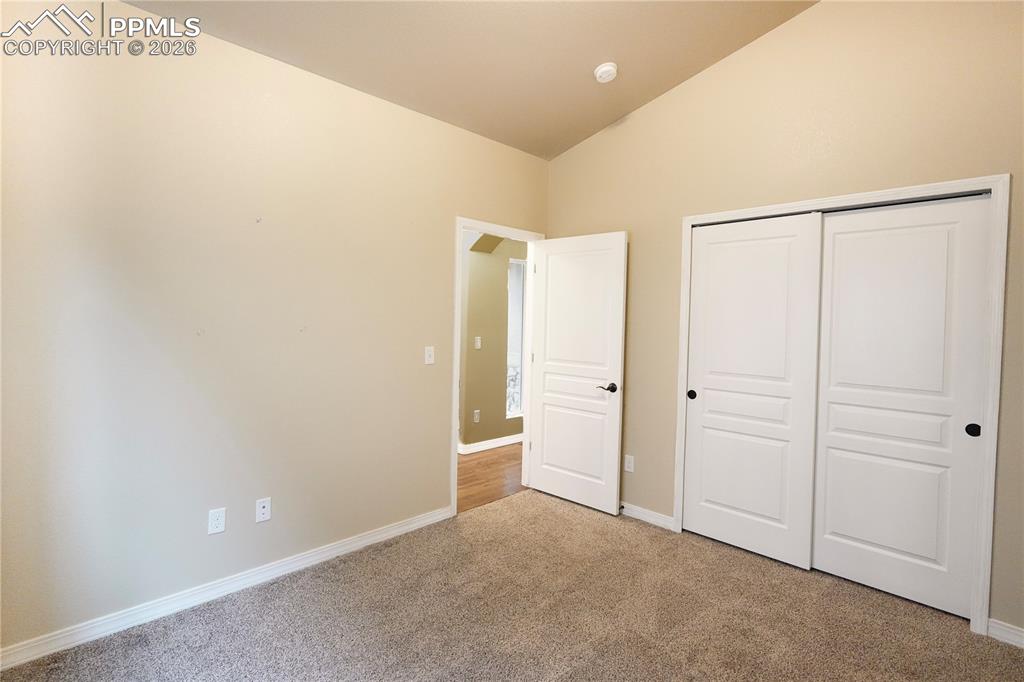 Unfurnished bedroom with light carpet, vaulted ceiling, and a closet