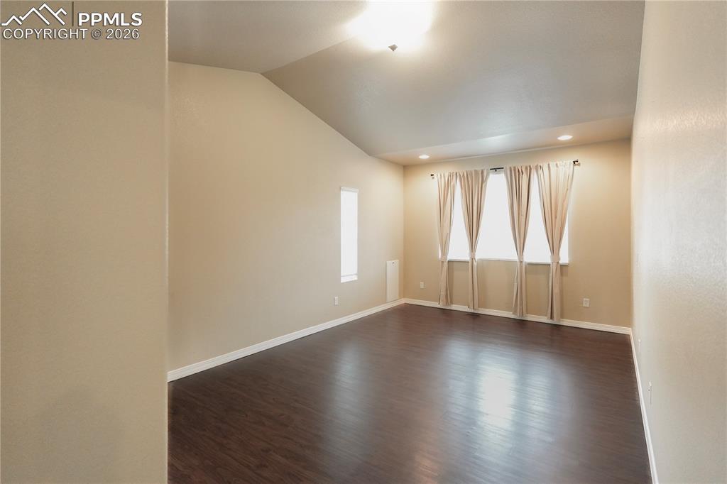 Empty room featuring dark wood-type flooring, lofted ceiling, and recessed lighting