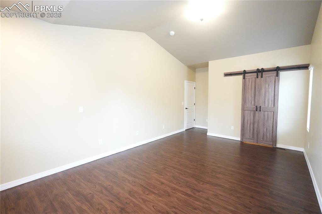 Unfurnished bedroom featuring a barn door, lofted ceiling, and dark wood-type flooring