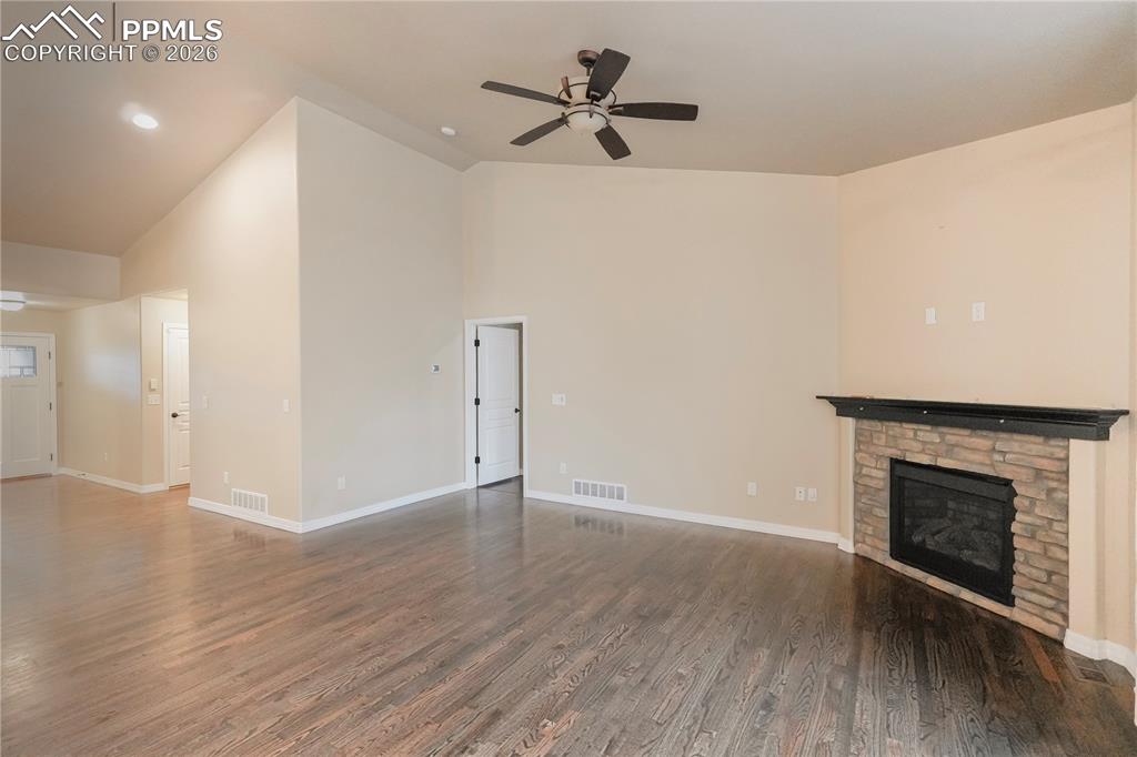 Unfurnished living room with ceiling fan, dark wood-style flooring, a stone fireplace, vaulted ceiling, and recessed lighting