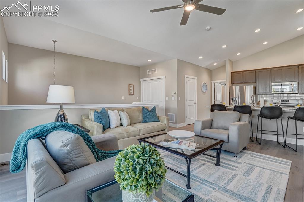 Living room featuring light wood-style flooring, ceiling fan, recessed lighting, and vaulted ceiling