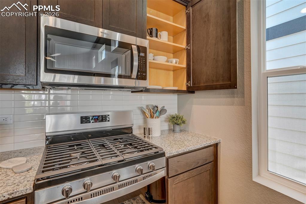 Kitchen with stainless steel appliances, light stone counters, tasteful backsplash, a textured wall, and dark wood finish cabinetry