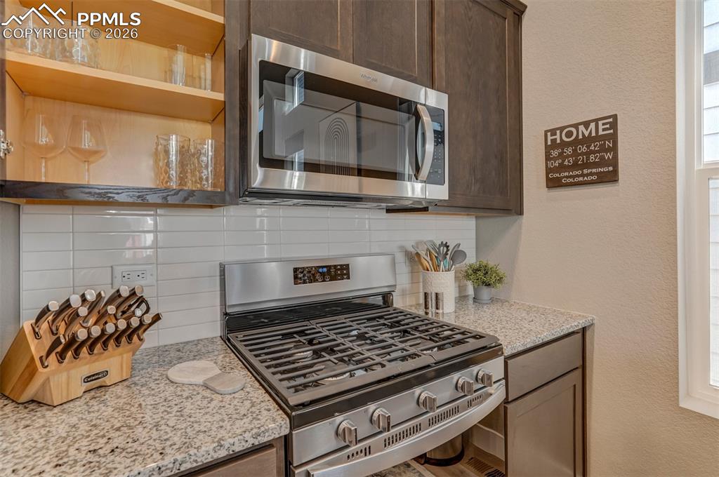 Kitchen with stainless steel appliances, a textured wall, light stone counters, backsplash, and dark wood finish cabinets