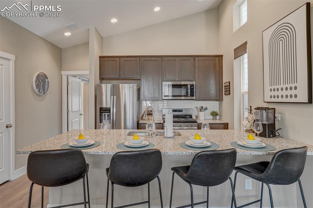 Kitchen with stainless steel appliances, a kitchen bar, light stone countertops, tasteful backsplash, and dark wood finish cabinets