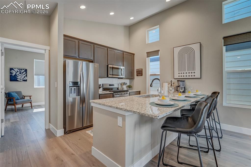 Kitchen featuring stainless steel appliances, light stone counters, a breakfast bar, dark wood finish cabinets, and light wood-type flooring