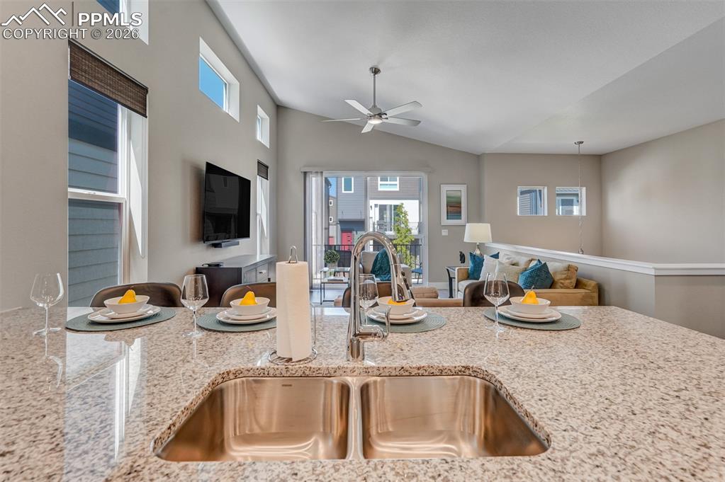 Kitchen featuring ceiling fan, open floor plan, light stone counters, and vaulted ceiling