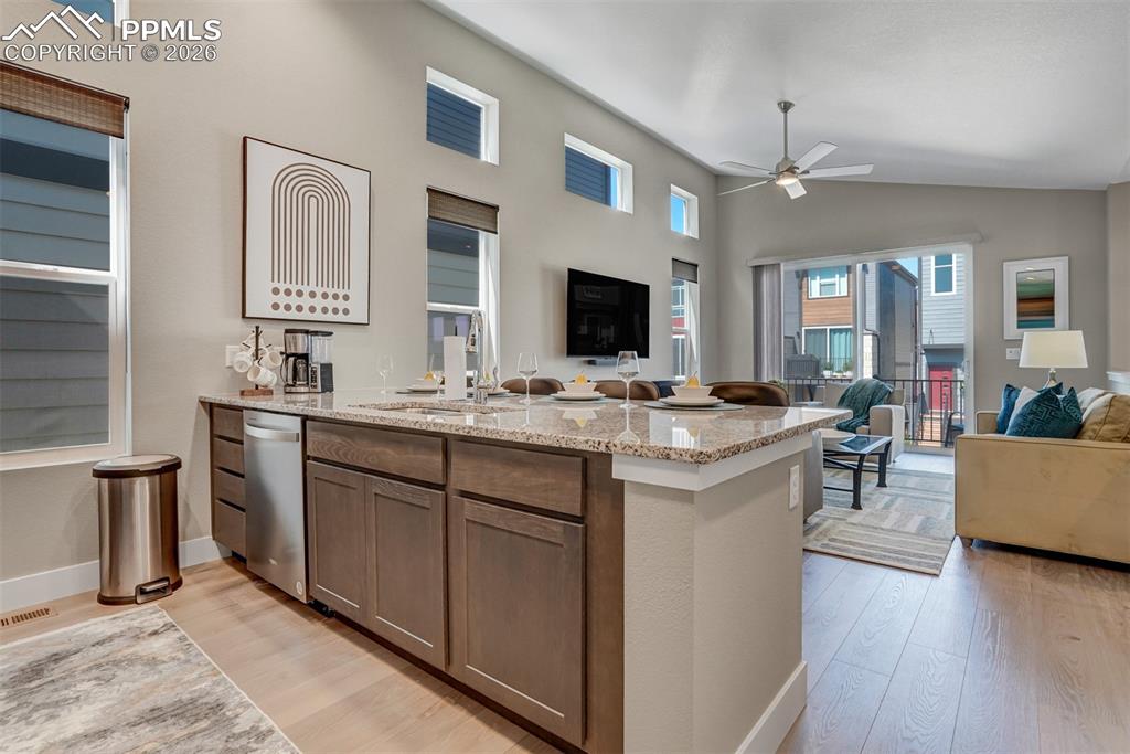 Kitchen featuring open floor plan, light stone countertops, light wood-style floors, and vaulted ceiling