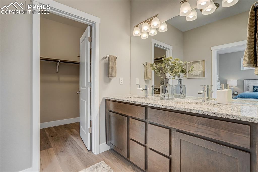 Ensuite bathroom featuring double vanity, light wood-style flooring, and a walk in closet