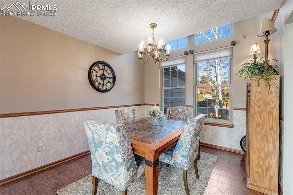 Dining area with hardwood floors, a textured ceiling, classic chandelier, and a wainscoted wall