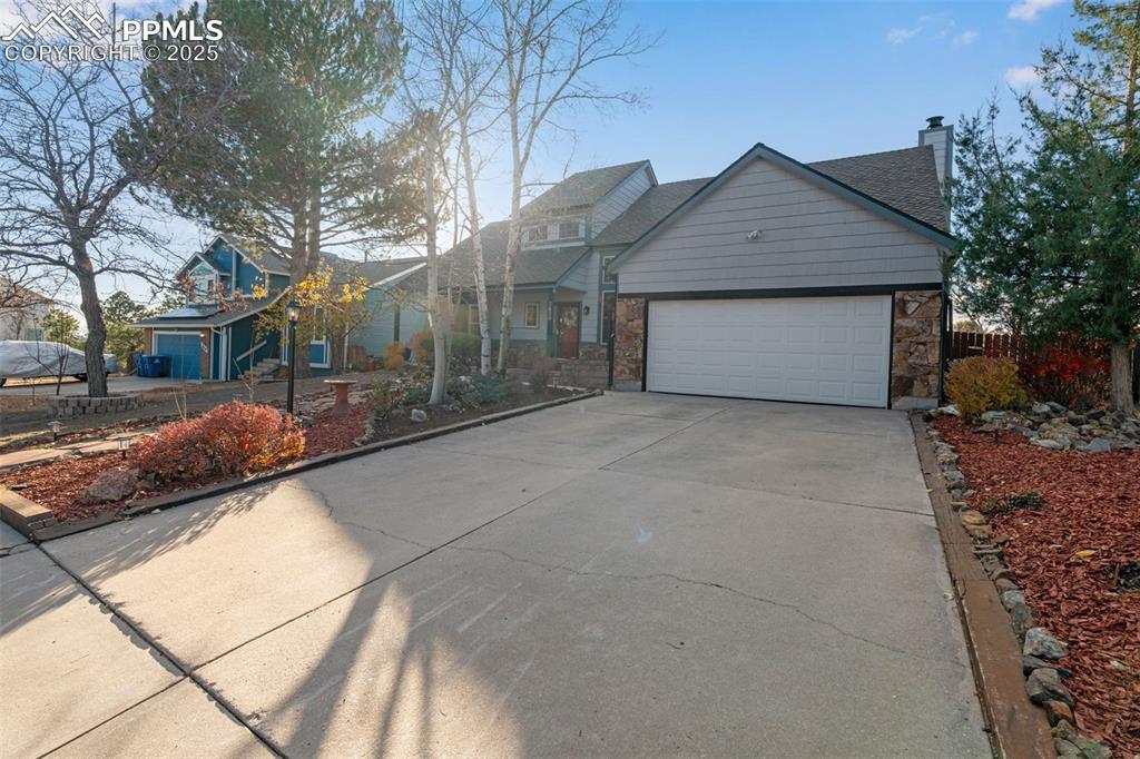 View of front facade featuring a chimney, concrete driveway, stone siding, and an attached garage