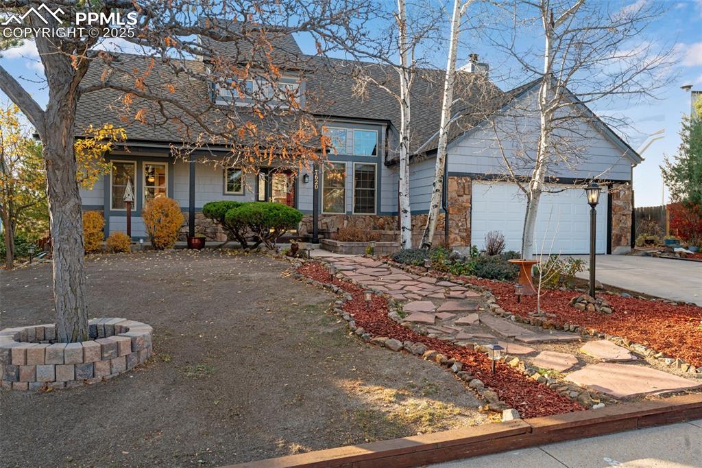 Traditional home with driveway, covered porch, roof with shingles, a garage, and a chimney