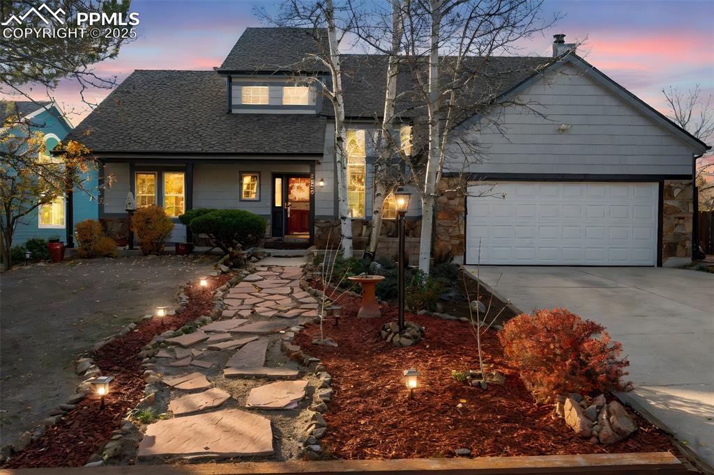 Traditional-style home with concrete driveway, roof with shingles, covered porch, an attached garage, and stone siding