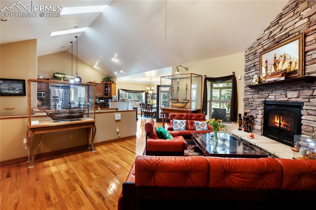 Living room with light wood finished floors, high vaulted ceiling, a chandelier, a fireplace, and three skylights. Overlooking the kitchen and the dining room.