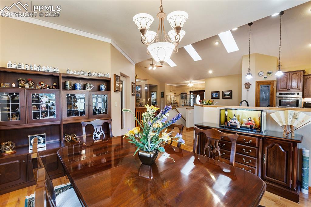 Dining room featuring light wood-type flooring, a chandelier, crown molding, and a high vaulted ceiling.