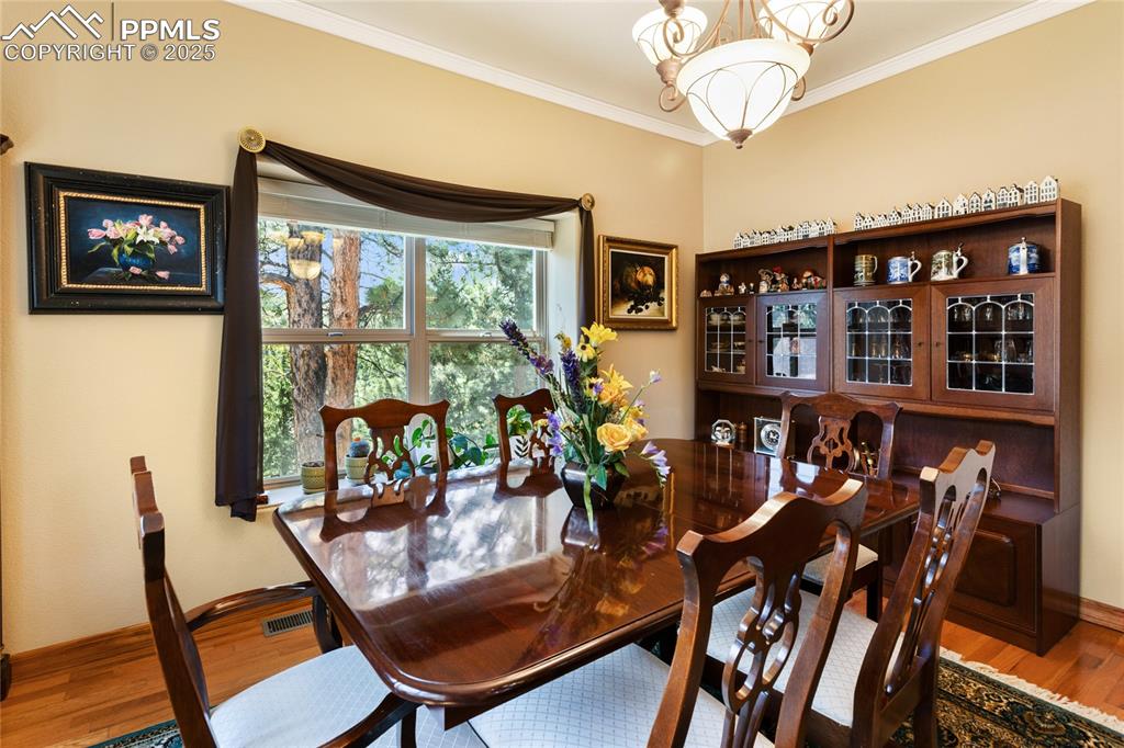 Dining area with ornamental molding, wood finished floors, and a chandelier. 