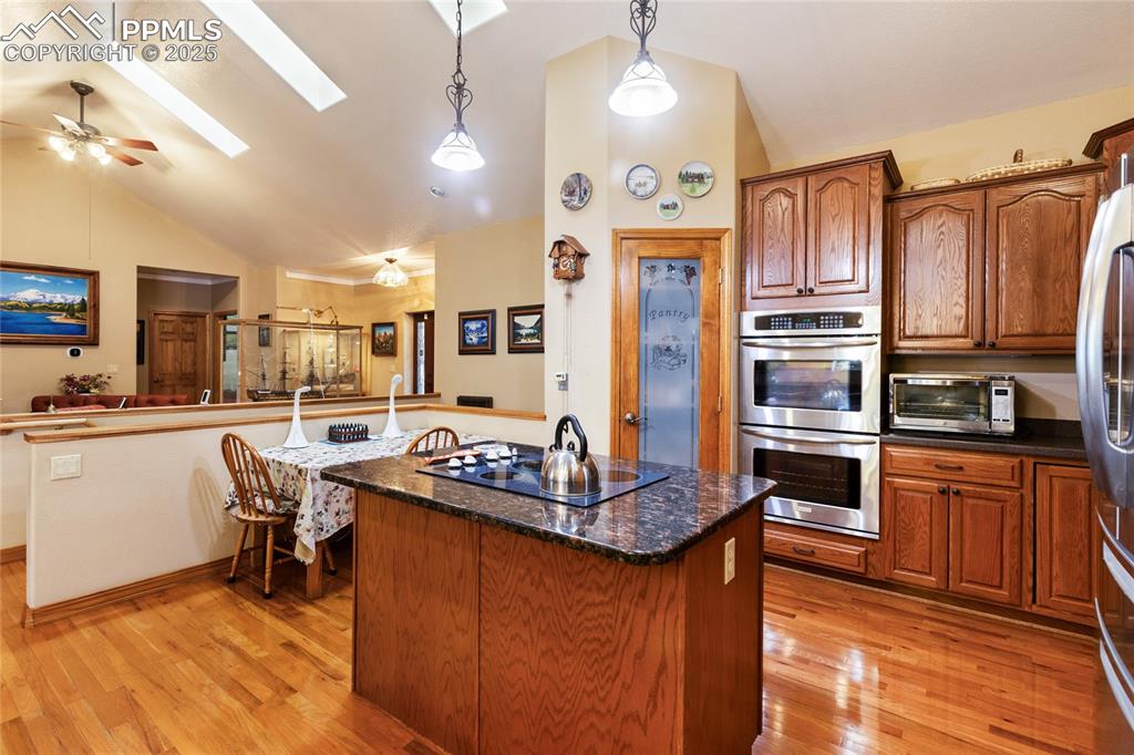 The kitchen features a lofted ceiling, pendant light fixtures, a three skylights, stainless steel appliances, a center island, and a pantry. 