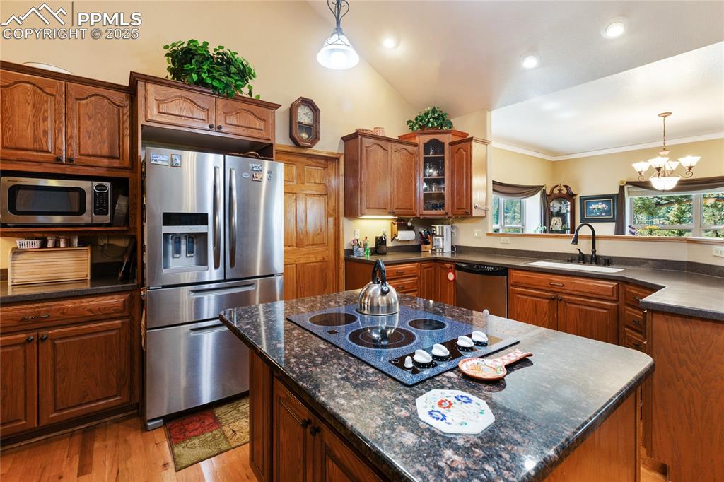 Kitchen featuring pendant lighting, stainless steel appliances, glass insert cabinets, and a kitchen island with an electric cooktop. 