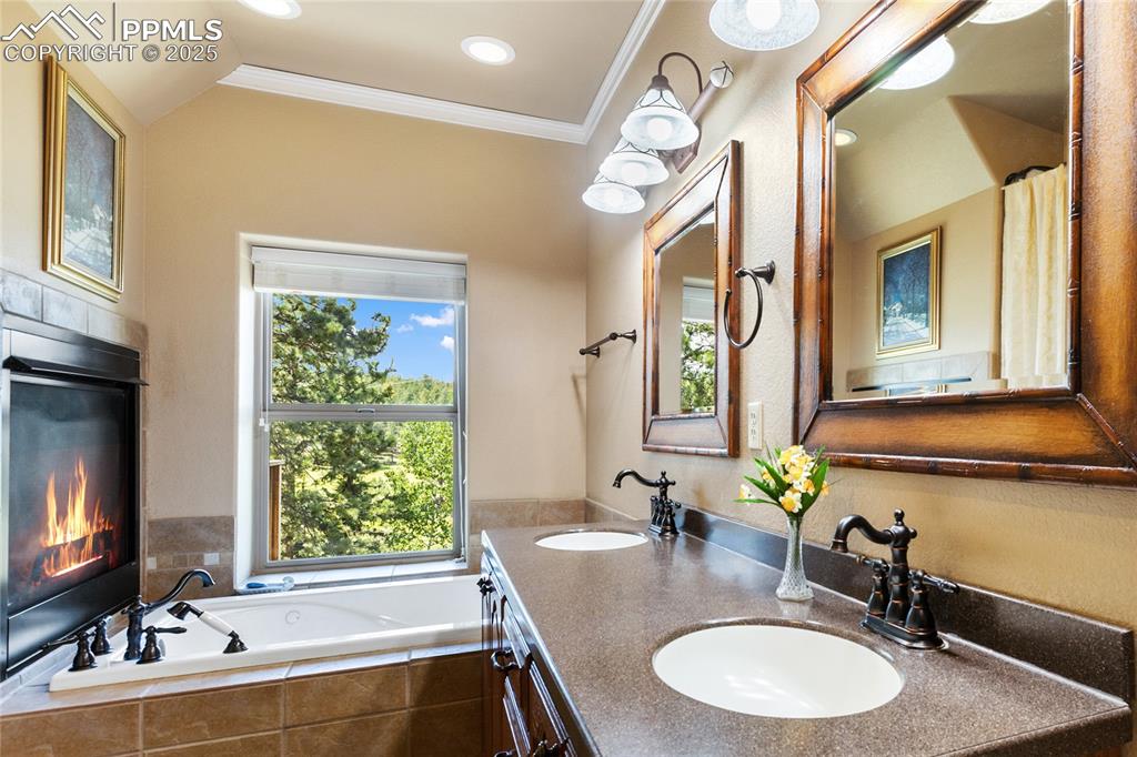 Bathroom with double vanity, a bath, ornamental molding, and a fireplace. 