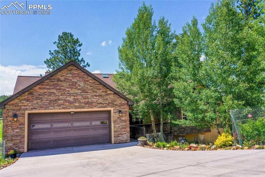 The front facade view showcases a garage, driveway, and stone siding.